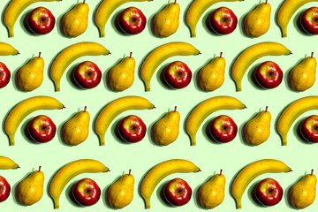 Fruit pattern. Repeating of whole bananas, red apples, and yellow pears on a light green background. Interesting fruit pattern made from natural fruits. Horizontal. The concept of healthy food 