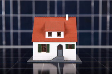 A small house model on a background of solar panels