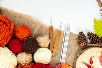 Cozy hobby concept for autumn. Balls of yarn (brown, red, orange, beige) for knitting, crochet hooks, knitting needles on sackcloth.