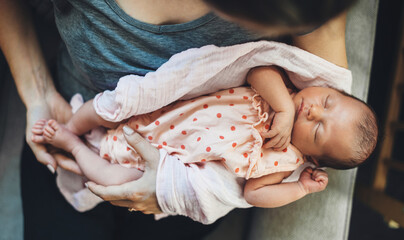 Caucasian woman holding his newbord daughter sleeping in her hands in a nice dress
