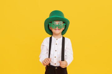 Smiling little child boy in green leprechaun hat on yellow background. St. Patrick Day celebration....