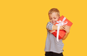 Studio shot of happy child boy celebrating holiday, unpacking gift box with excited face, posing...