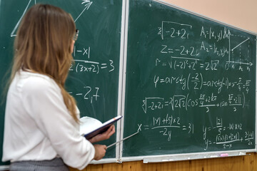 Young college student writing mathematical exercise on the chalkboard during a class