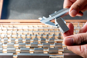The inspector is calibrating a vernier caliper micrometer with a gauge block. A small number of...