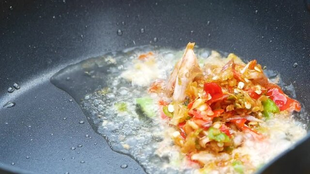 Close up of woman's hands cooking stir fried chilli peppers and garlic in a frying pan on hot fire from gas in kitchen. Delicious Thai food. Stir Fried Pork with Basil Leaves.