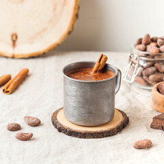 Hot chocolate in a metal mug with a cinnamon stick on the tablecloth. Copy space