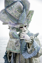 Person wears carnival mask and ornate blue costume with toy owl on his hand posing at Carnival in Venice celebration, Italy