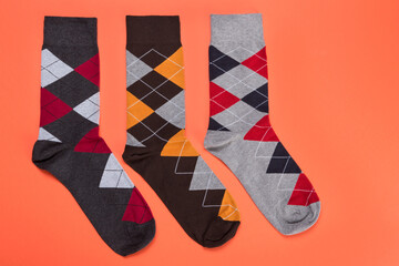 three socks with color patterns of rhombuses lined up in a row on an orange background, concept