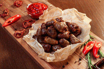 Fried chicken hearts with vegetables and spices on a wooden board.
