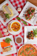 Flat lay shot of delicious italian cuisine. Delicious pizza, salmon rolls, pumpkin soup and salad on a wooden table.
