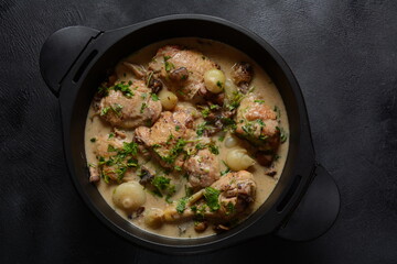 Fricassee - French Cuisine. Chicken stewed in a creamy sauce with mushrooms in a black dutch oven on a black table 