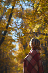 Portrait of a young happy beautiful woman in a brown hat and red plaid walks in the autumn sunny park at sunset. Inspiration, autumn mood, travel, beauty of nature, forest.