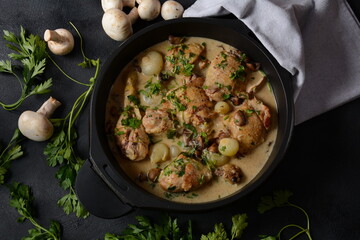 Fricassee - French Cuisine. Chicken stewed in a creamy sauce with mushrooms in a black dutch oven on a black table 