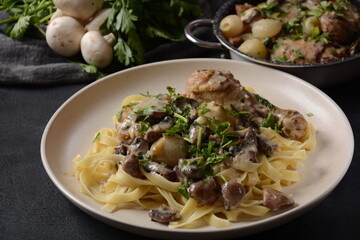 Fricassee - French Cuisine. Chicken stewed in a creamy sauce with mushrooms in a white plate on a black table 