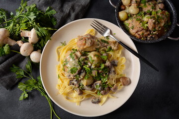 Fricassee - French Cuisine. Chicken stewed in a creamy sauce with mushrooms in a white plate on a black table 