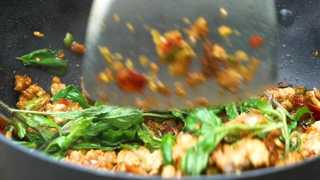Close up of woman's hands cooking stir fried chilli peppers and garlic with minced pork in a frying pan on hot fire from gas in kitchen. Delicious Thai food. Stir Fried Pork with Basil Leaves.
