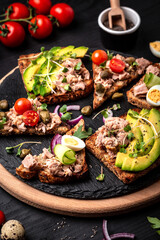 Set Toasts with tuna. Italian bruschetta sandwiches with canned tuna, quail egg, cherry tomatoes, avocado, microgreen and capers Delicious breakfast or snack. Top view