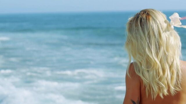 Back shot of blonde model walking in her bikini by the sea.