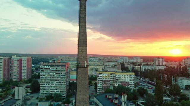aerial view multi storey apartment buildings in residential area of city on beautiful colorful sunset sky with clouds and down sun. large tall old brick chimney in the foreground