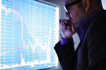A businessman is looking at a graph on a monitor. An exchange broker evaluates stock market trends....