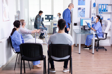 Disabled senior woman with walking frame sitting in hospital waiting area for medical consultation against infection with coronavirus. Social distancing, medic, covid-19, man, worried, protection,