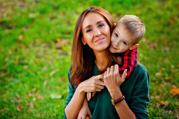 Obraz premium Large portrait of a young mother and son in the Park. happy family: a mother and boy play cuddling on an autumn outdoor nature walk.