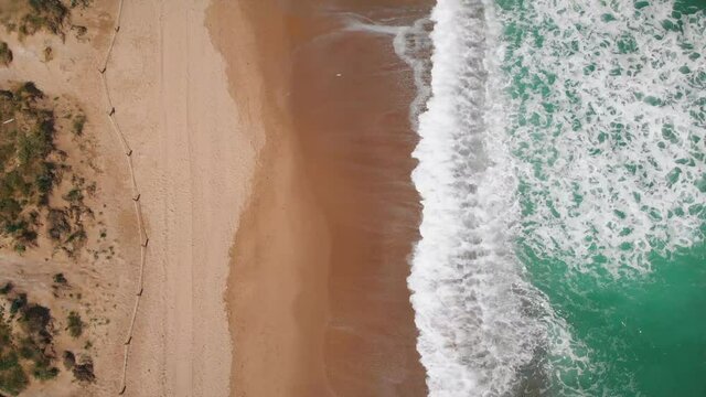 4K Aerial view top down of Beautiful beach with white sand and foaming waves crushing against coast line. Saler Beach, Valencia, Spain