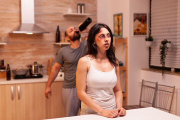 Violent husband drinking alcohol after beating wife. Woman bruised because of domestic violence....