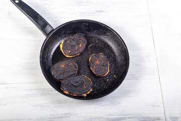 the wooden background is painted white. There is a frying pan and fried pancakes on it. Close-up.