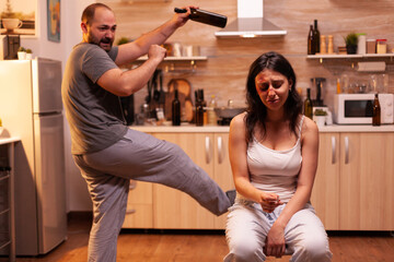 Depressed woman because of domestic violence smoking on chair. Violent aggressive man abusing...
