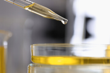 Dispenser filled with yellow chemical liquid pours drop into a glass dish closeup. Providing...