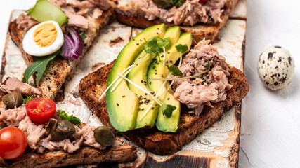 Set Tasty tuna sandwiches with quail egg, cherry tomatoes, avocado, microgreen and capers. Delicious breakfast or snack