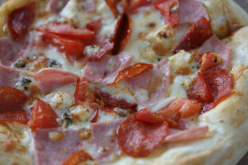 Pizza with cheese, ham, sausage, spices and tomato sauce closeup. Unhealthy fast food concept.