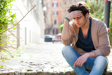 Anxiety. Thoughtful young man anxious, outdoors. A young and handsome boy is sitting on the street...