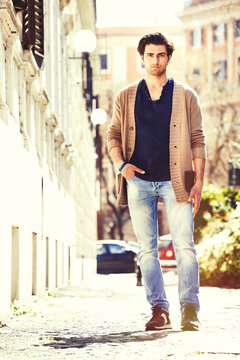 Gorgeous men outdoors, urban scene in the city. He stands walking on a street near a historical palace.