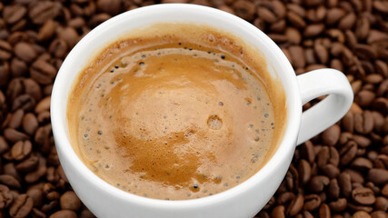 a cup of black coffee with froth on coffee beans top view