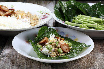 Traditional Thai Betel leaf wrapped with fish meat minced and cutting grilled fish sausage serving with chilly and fresh bean on the plate. Famous Thai royal ancient snack menu.