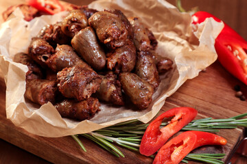 Fried chicken hearts with vegetables and spices on a wooden board.