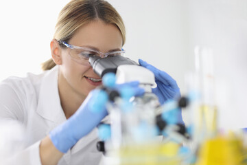 Woman in rubber gloves and protective chemical glasses looks through microscope in laboratory portrait. Conducting clinical diagnostic analyzes concept.