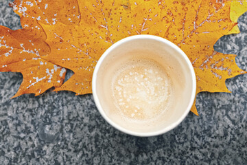 cup with leftover cappuccino coffee and yellow autumn maple leaves on marble background, copy space