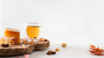 Autumn hot tea with ginger and cinnamon in a glass tea cup, honey combs and autumn leaves on a wooden tray on white background. Copy space. Cozy fall concept, hygge banner