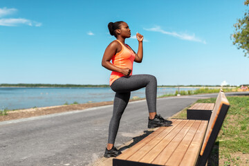Fototapeta na wymiar fitness, sport and healthy lifestyle concept - young african american woman exercising with bench at seaside