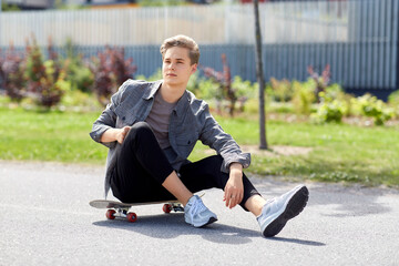 people and leisure concept - young man or teenage boy sitting on skateboard on city street © Syda Productions