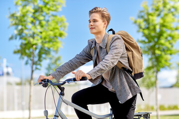 lifestyle, transport and people concept - young man or teenage boy with backpack riding bicycle on...