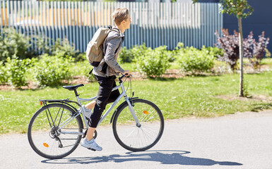 lifestyle, transport and people concept - young man or teenage boy with backpack riding bicycle on city street