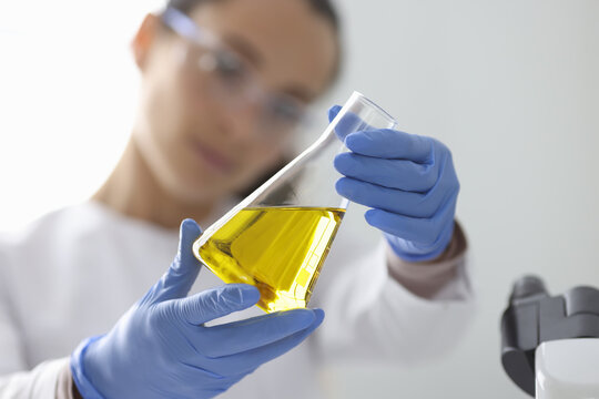 Female hands in rubber gloves holding flask with urine analysis in clinical laboratory closeup. Research on quality of oil products concept.