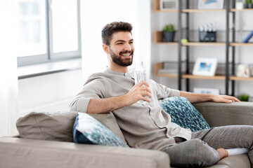 people, sustainability and leisure concept - happy smiling young man sitting on sofa and drinking...