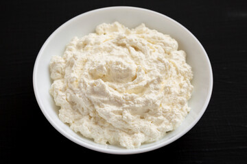 Tasty Ricotta Cheese in a white bowl on a black surface, low angle view.