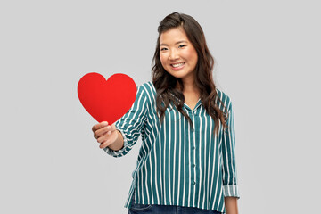 love, charity and valentines day concept - happy asian young woman with red heart over grey background