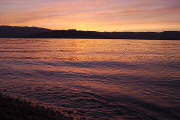 Fototapeta na wymiar 夕暮れの湖。穏やかな波の水面に映る空の色。遠くの山のシルエット。